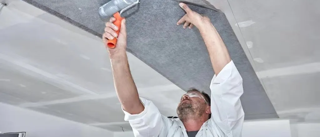 An installer rolling a ComfortScrim infrared heating element onto a ceiling before it is plastered over