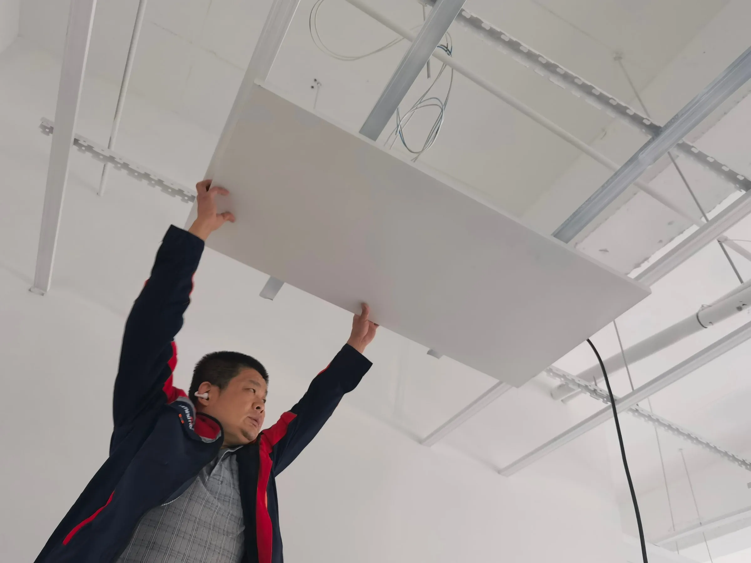 An installer lifting a PowerBoard panel into a ceiling grid