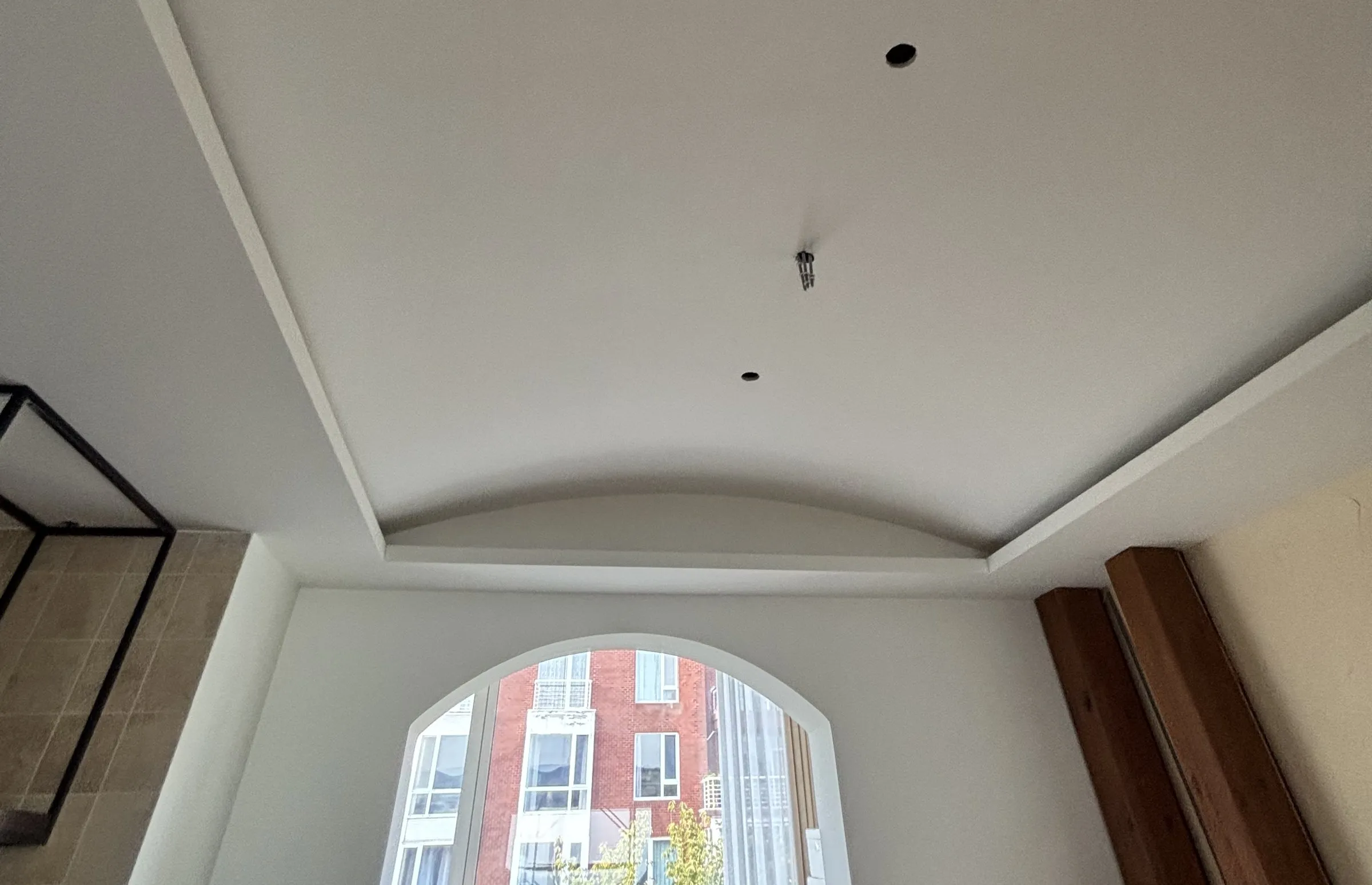 A curved dining-room ceiling in a Qingdao villa, painted plain white, above an arched window