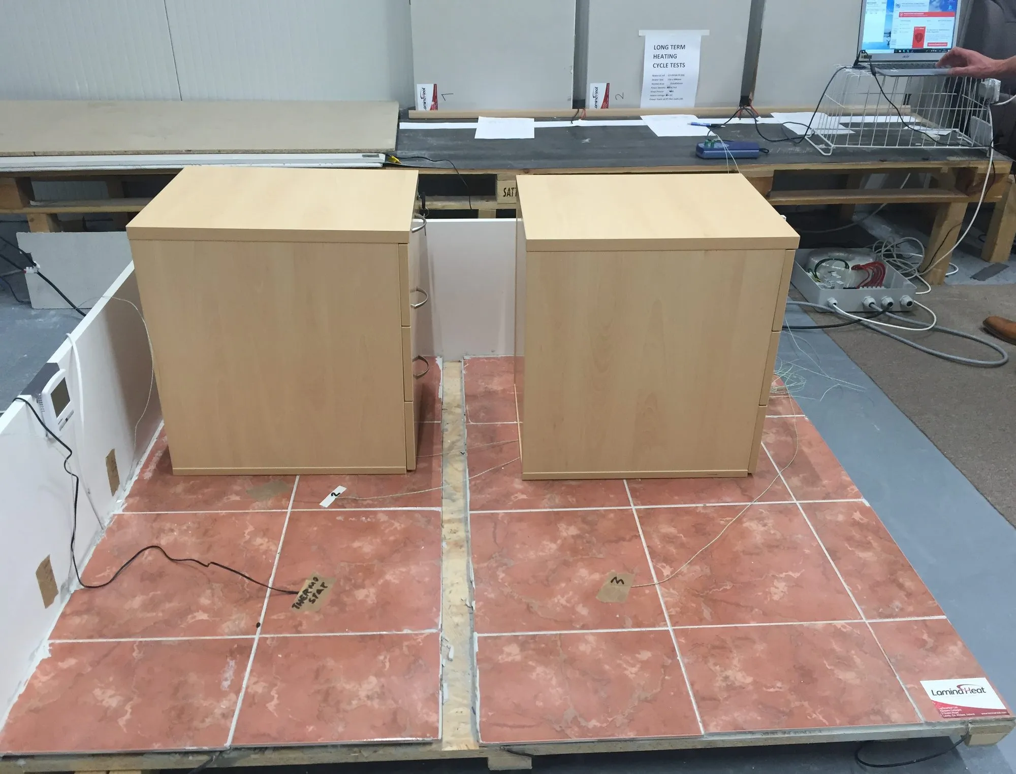 The test floor: two halves of ceramic tile on a timber base, a heating cable under the left half and full-surface film under the right half, with a data logger in the background