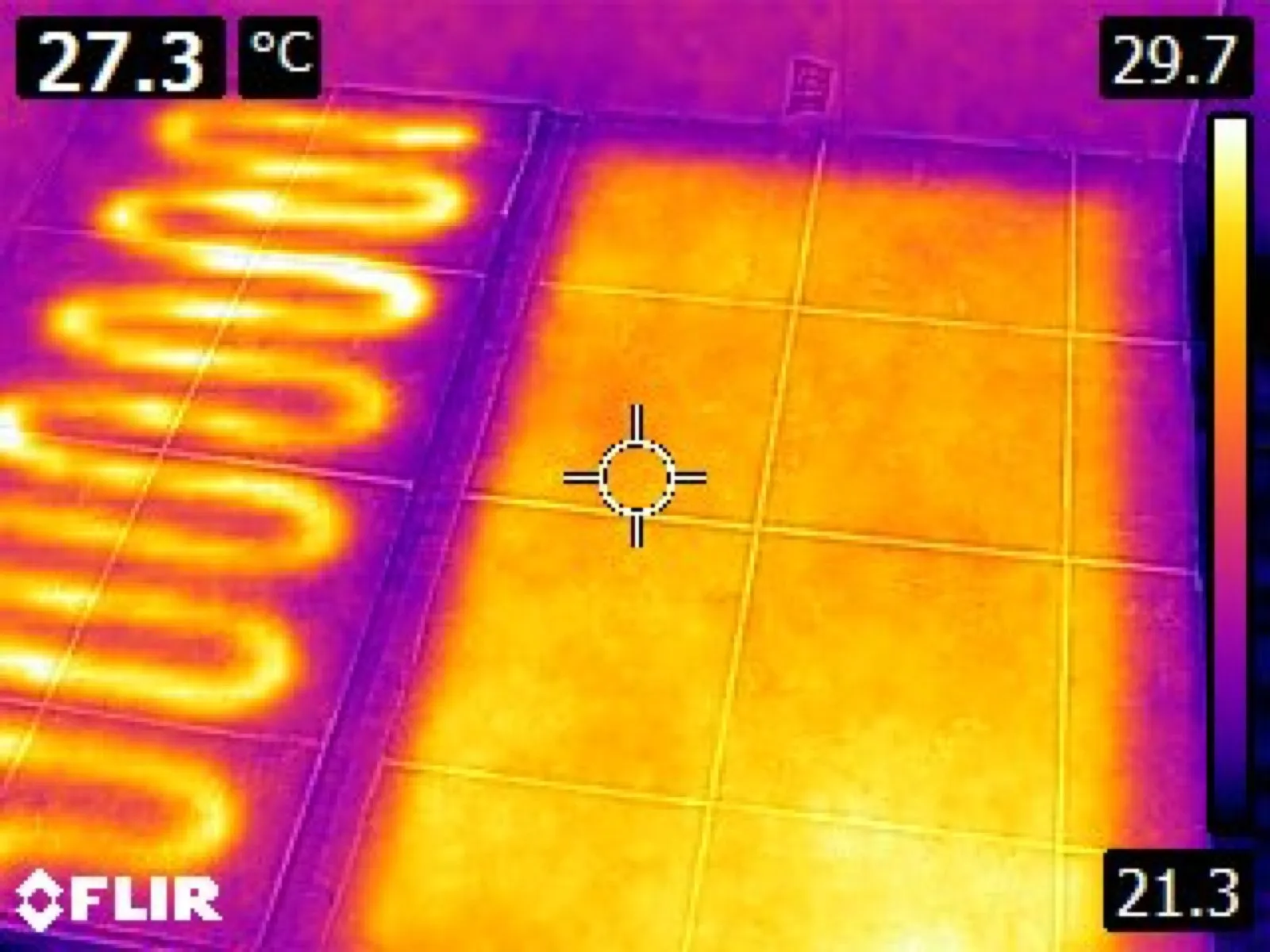 Thermal camera image of a tiled test floor: on the left, bright stripes where a heating cable runs, with cooler tile between them; on the right, full-surface film warming the whole tiled area evenly