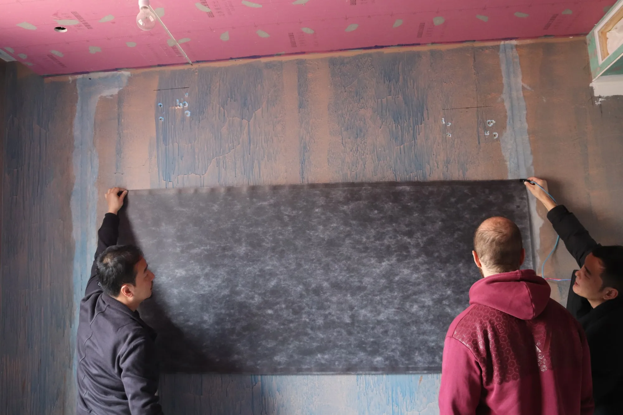 Two installers fitting a length of ComfortScrim to a wall